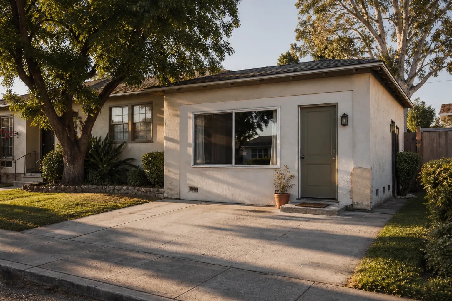 A converted garage on a Los Angeles bungalow, its roll-up door replaced by a stucco wall with a wide window and its own front door, the original driveway apron still running up to it