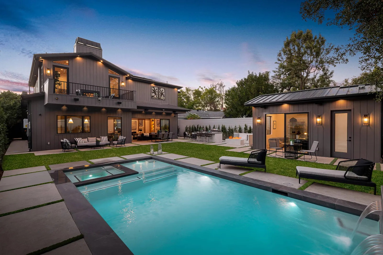 Backyard with a pool, spa and detached backyard unit at dusk